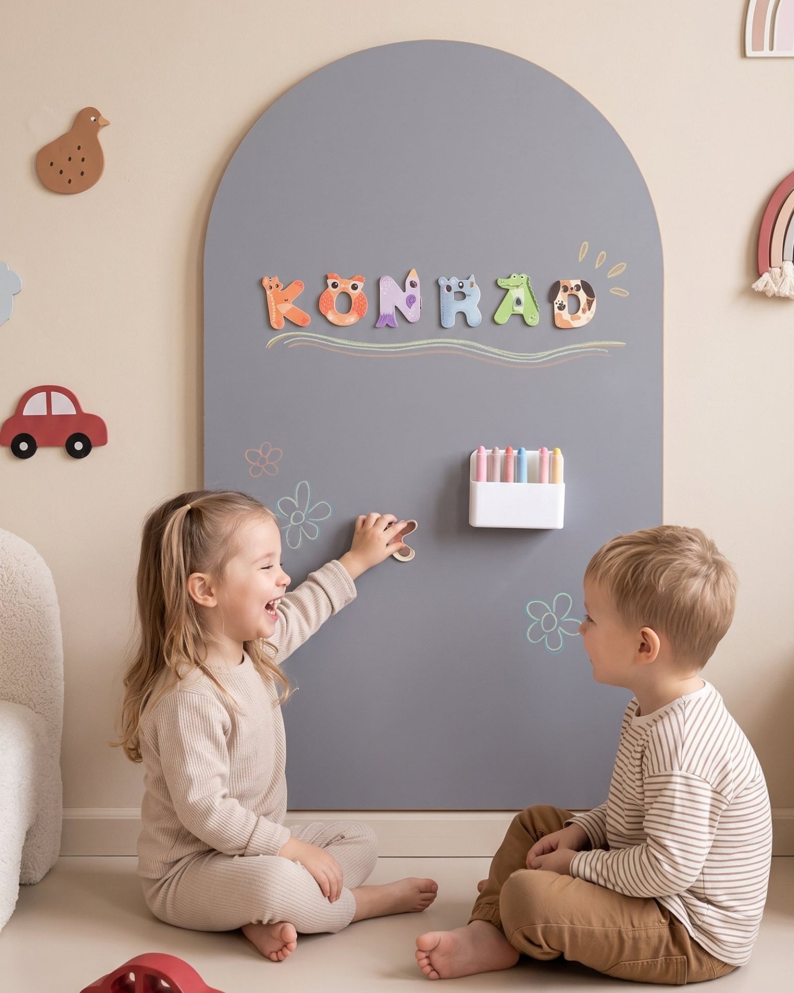Meisje en jongen spelen op de vloer voor de MagneetBoog+ in Maanestof (grijs) met lettermagneten en krijttekeningen