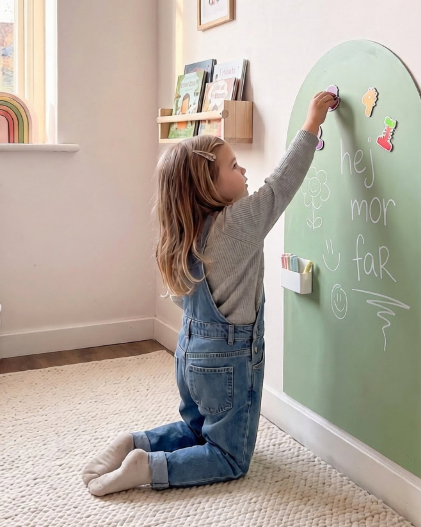 Meisje op knieën plaatst magneten op MagneetBoog+ in Noorderlicht (stofgroen) met krijttekst "hallo mama papa"